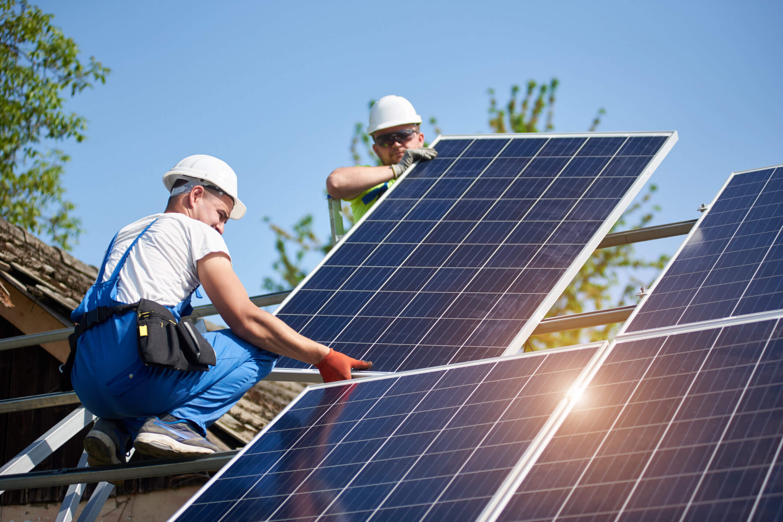Man with hard hat and orange vest assembles solar panel in the mountains