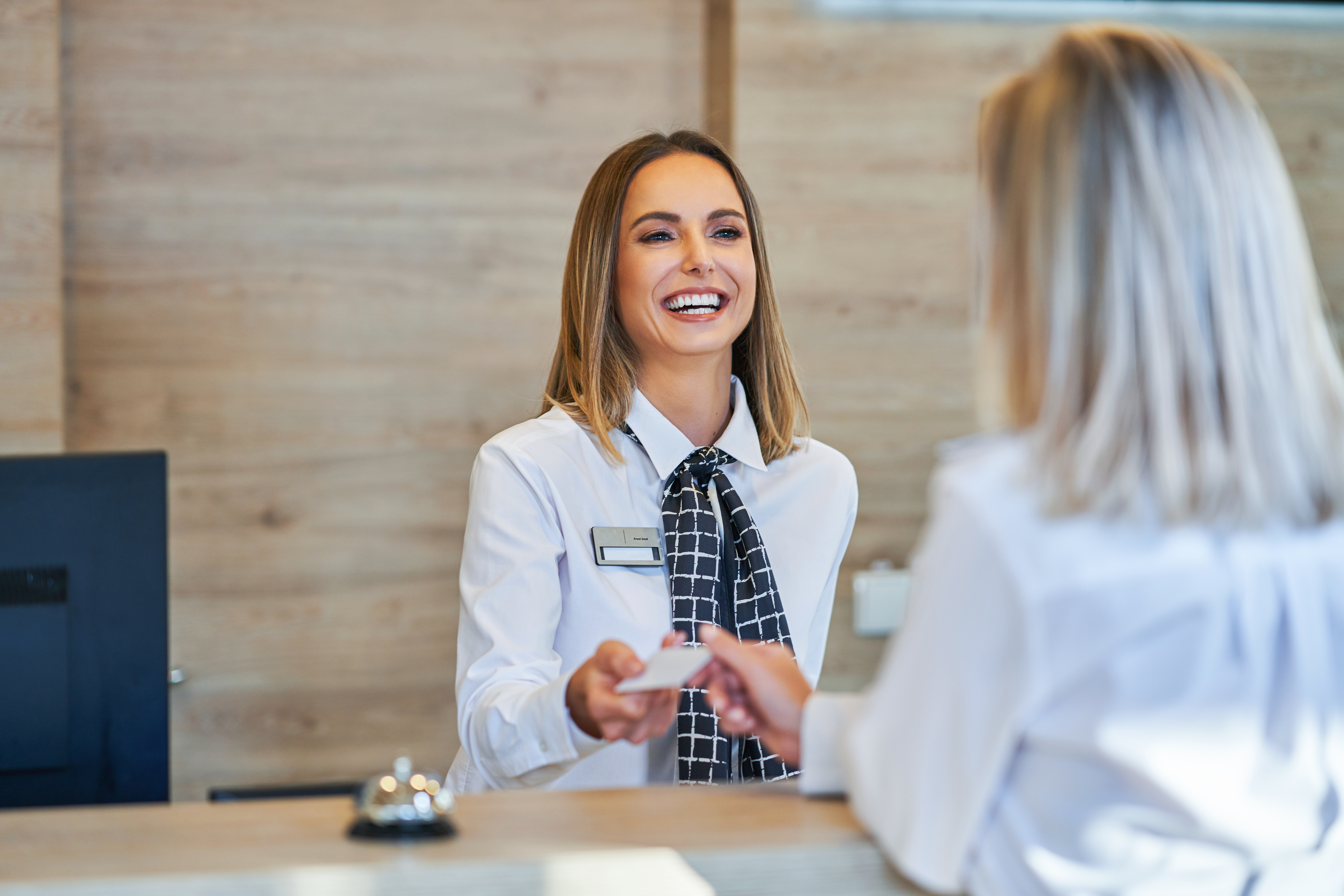Female receptionist smiling and handing room key to businesswoman at hotel front desk