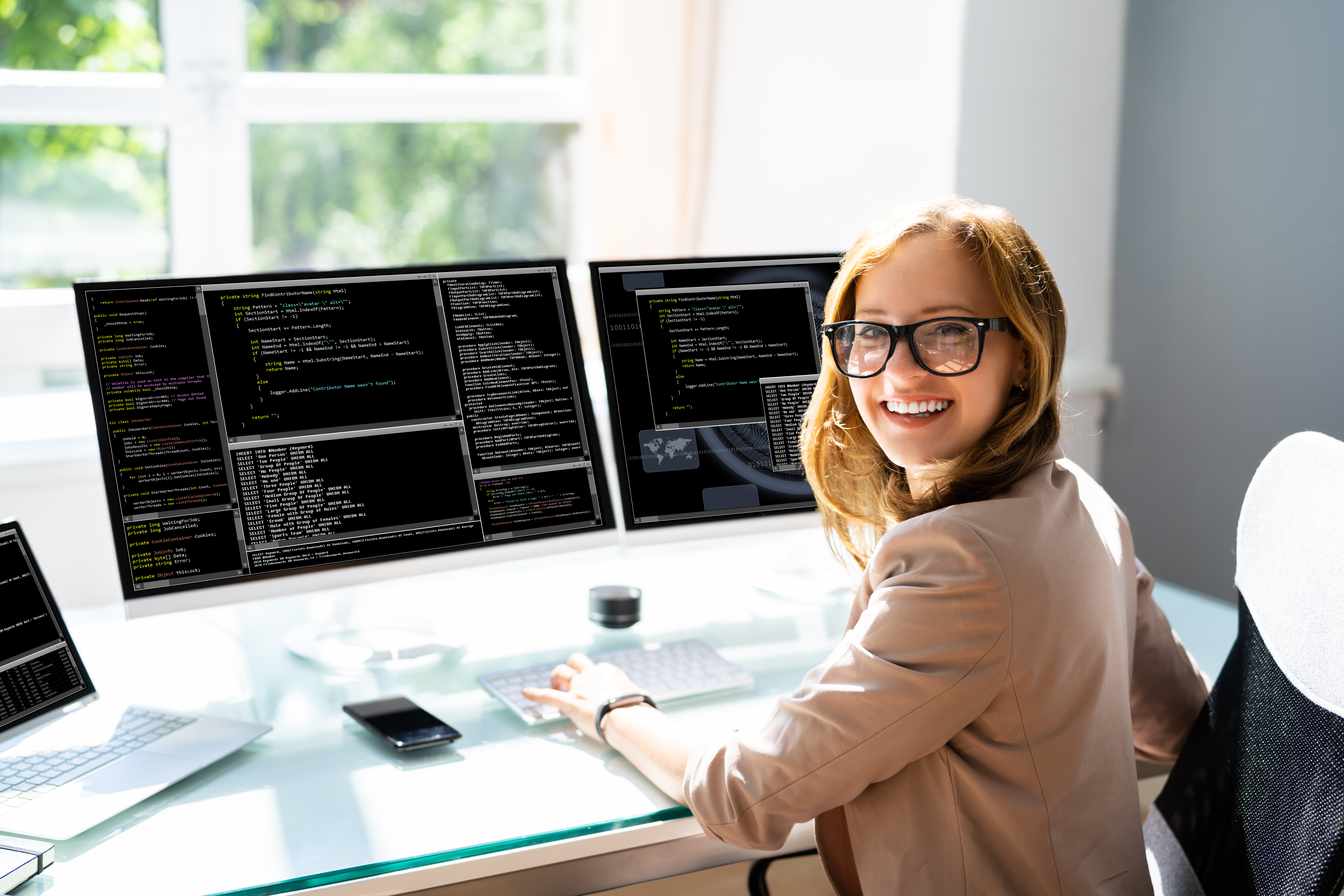 Female programmer smiling in front of two computer monitors with code